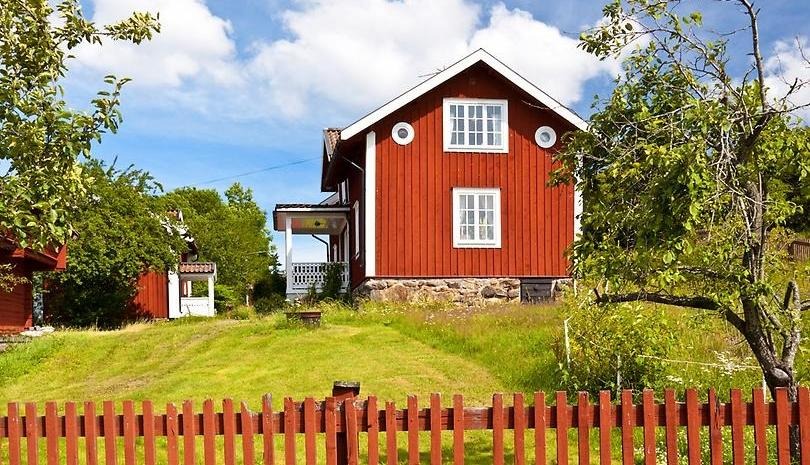 Rött hus med vita knutar i sommarmiljö.
