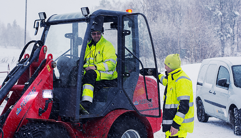 Två vaktmästare en vinterdag. En sitter i en traktor, den andra står bredvid.