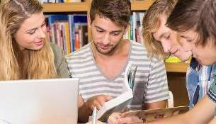 En tjej och tre killar läser bok framför dator.