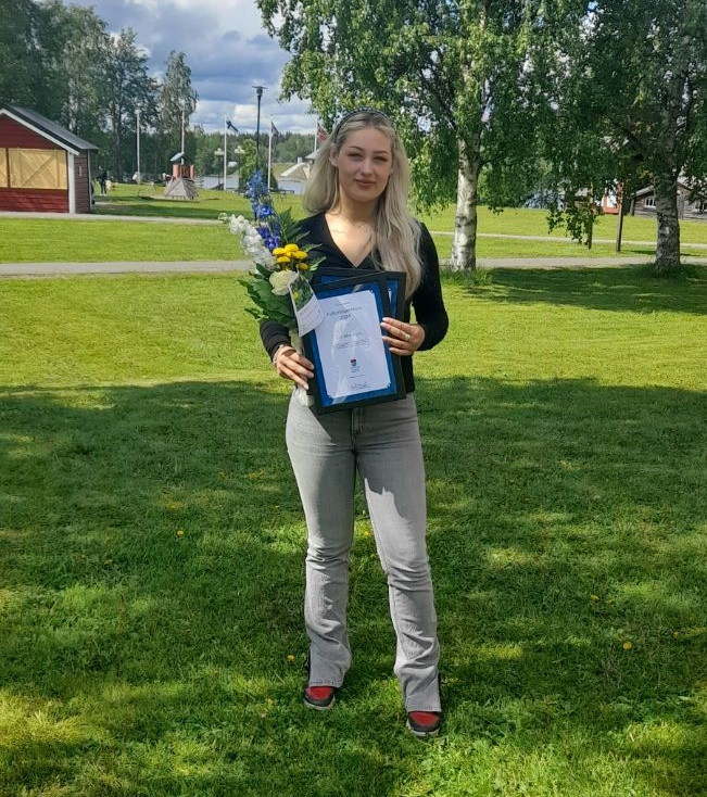 Ung kvinna som håller i blommor och ett diplom.
