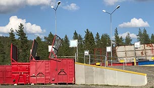 Röda containar och skyltar vid återvinningsstation.