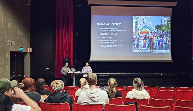 Två personer föreläser, publik i förgrunden.