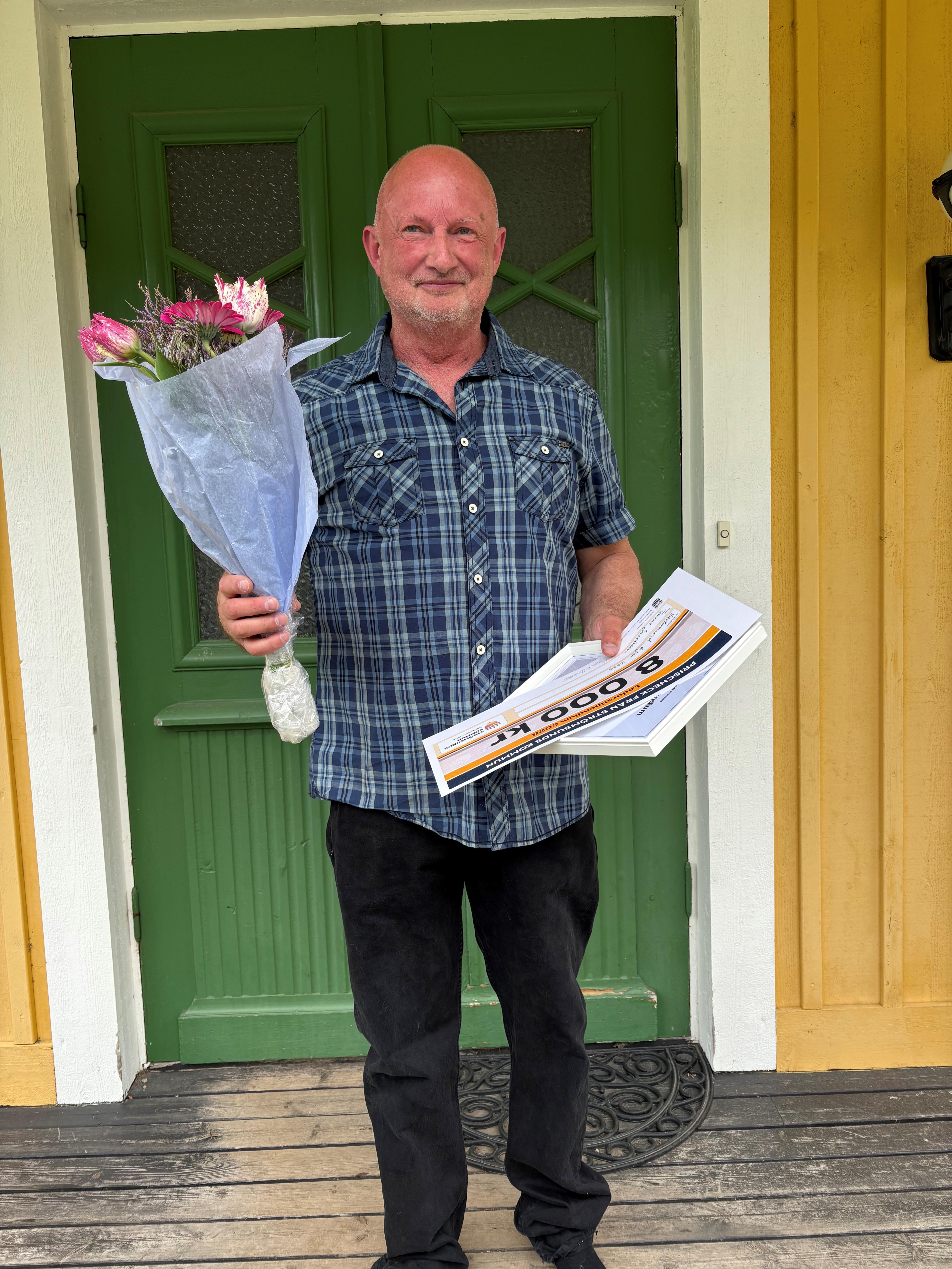 Bild på ledarstipendiat framför en grön dörr, håller en blombukett i ena handen och en check i den andra