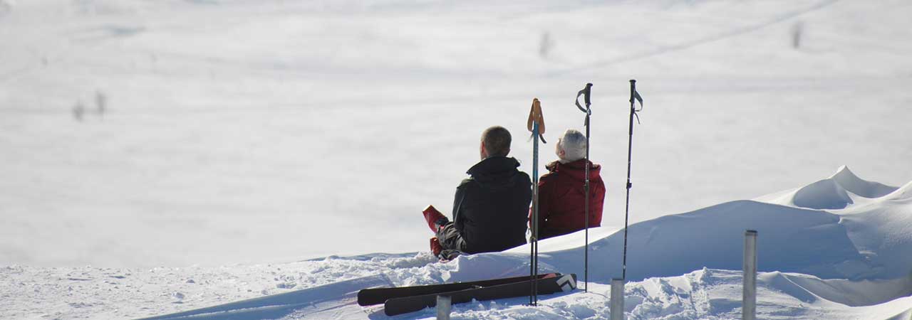 Par med skidor sitter i snödriva och solar.