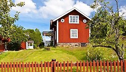Rött hus med vita knutar i sommarmiljö.