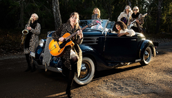 Sex kvinnor med instrument sitter och står runt en bil.