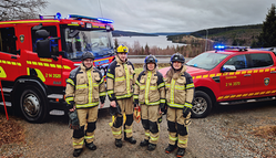 Fyra deltidsbrandmän. I bakgrunden vy över Frostviken samt en brandbil och ett räddningsfordon. 