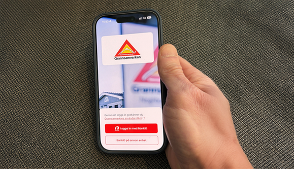 Närbild av hand som håller i mobiltelefon. Text på skärmen: Grannsamverkan. 